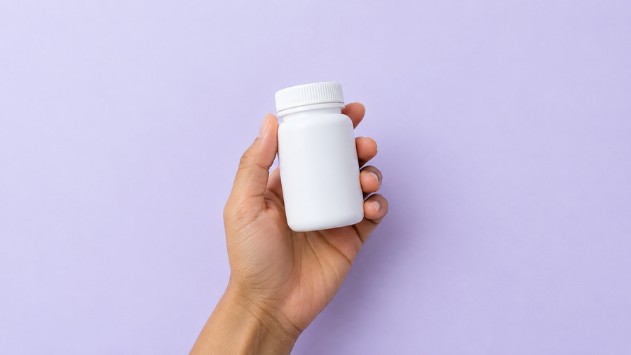 A hand holding a small plain supplement bottle