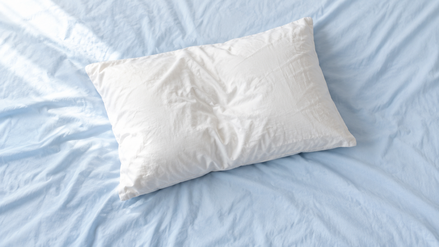 A rumpled pillow on a light blue bedsheet in morning light